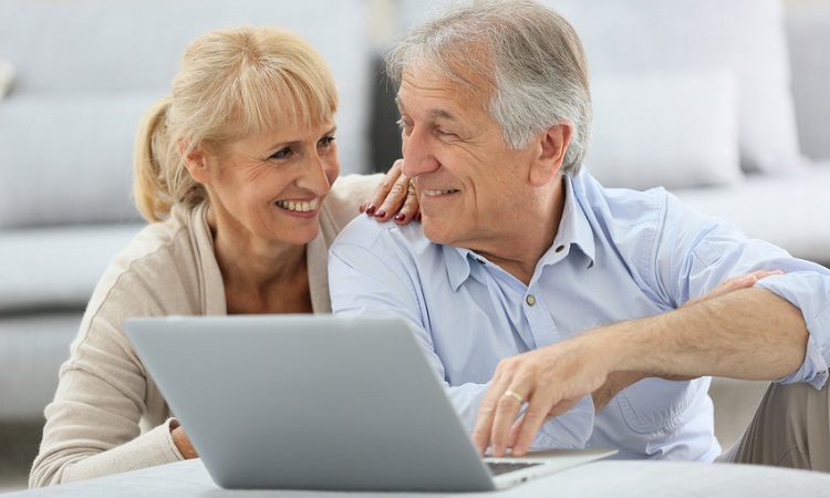 Zwei Senioren sitzen vor Laptop und surfen im Internet. 